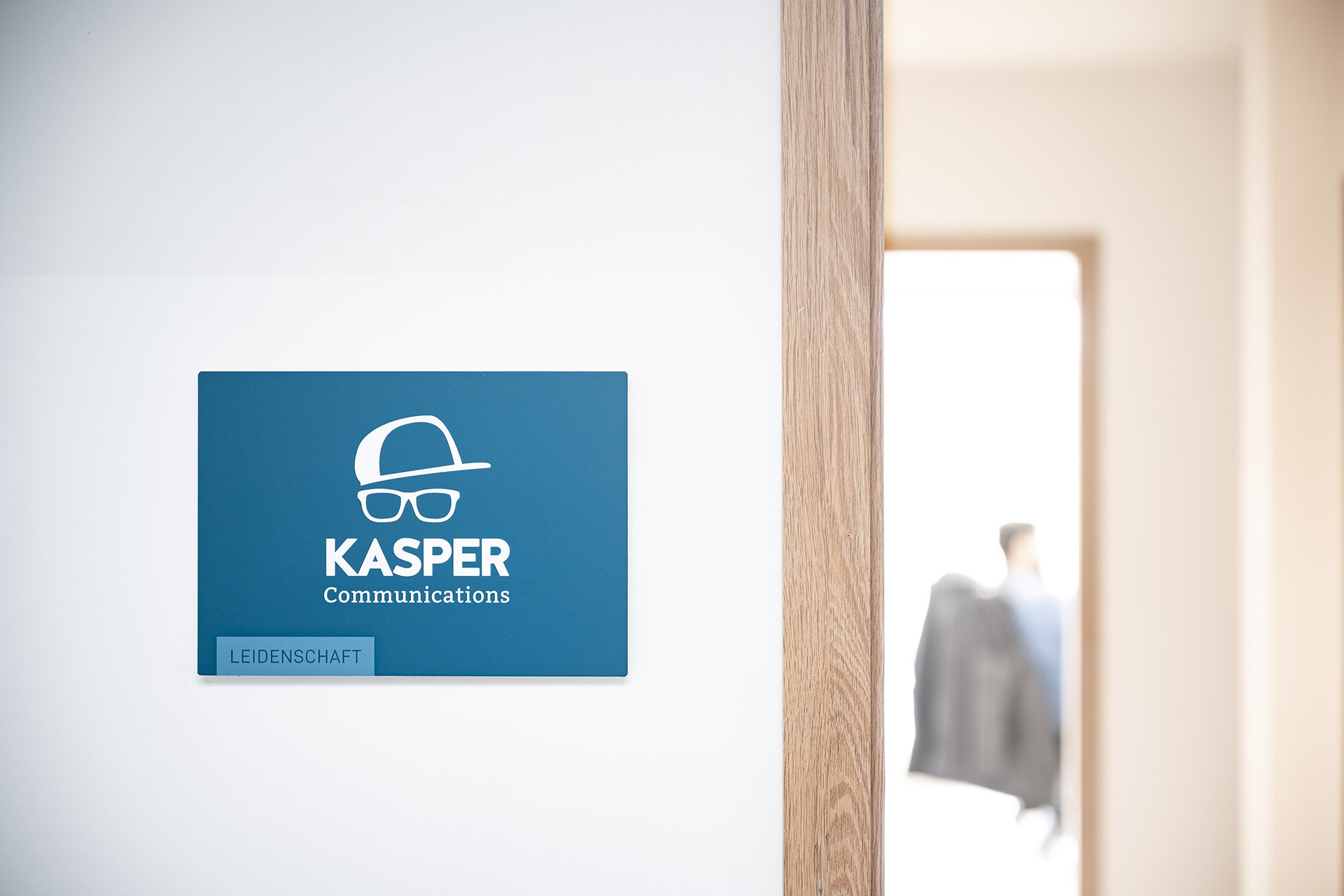 Türschild von Kasper Communications mit Logo und Schriftzug 'Leidenschaft'.