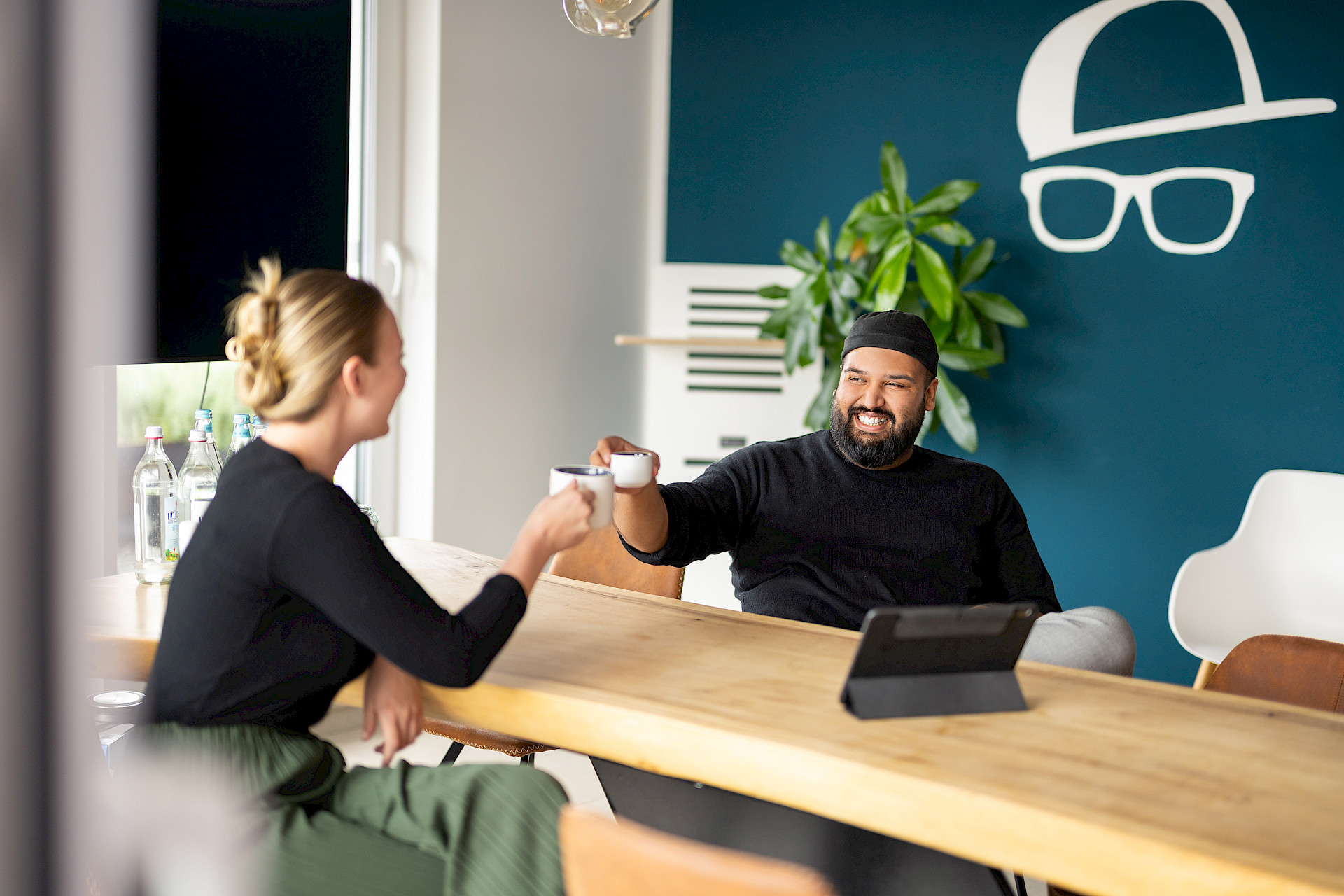 Zwei Personen stoßen mit Kaffeetassen in einem modernen Büro an.