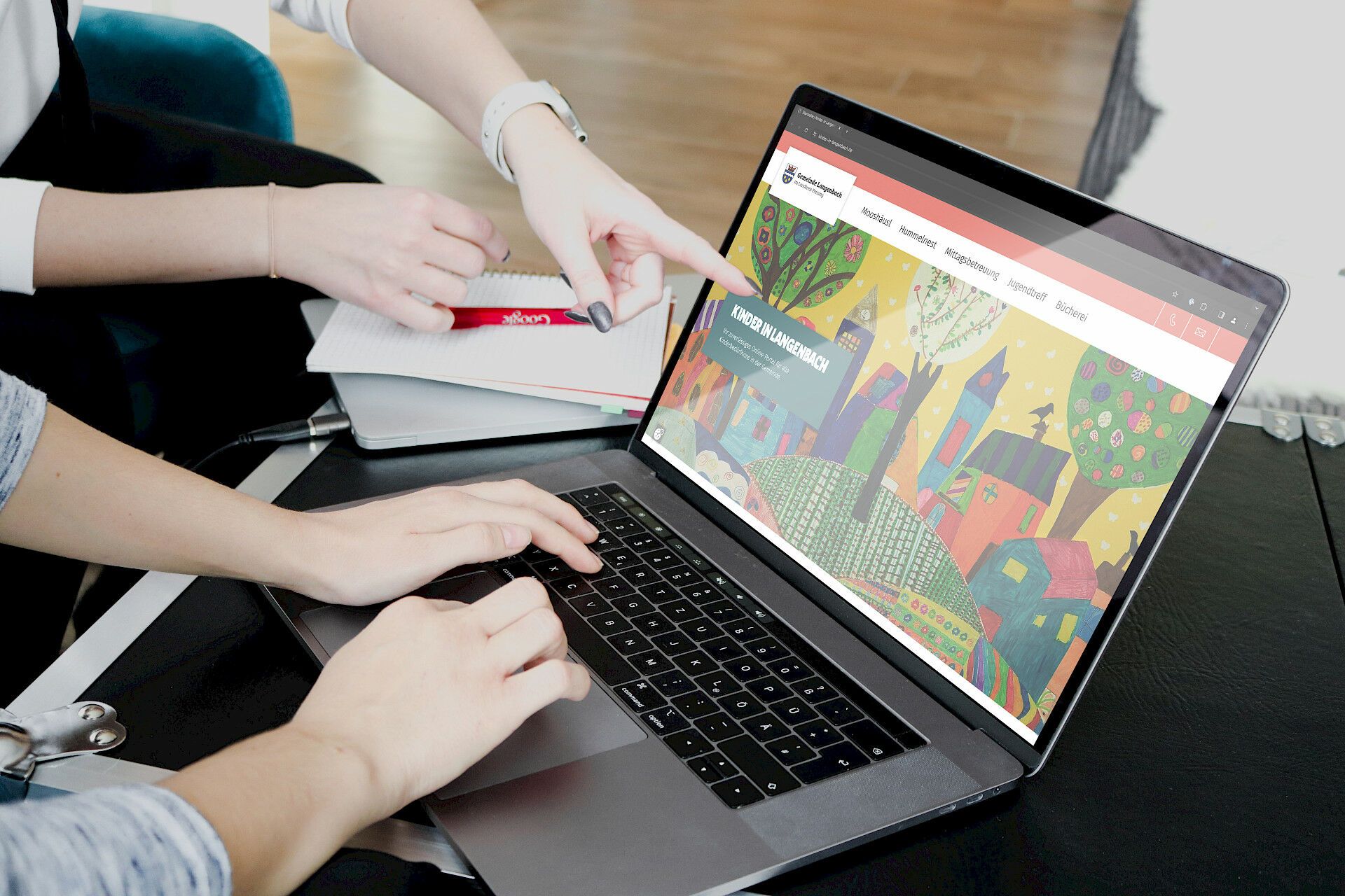 Personen arbeiten gemeinsam an einem laptop und eine person zeigt auf den bildschirm