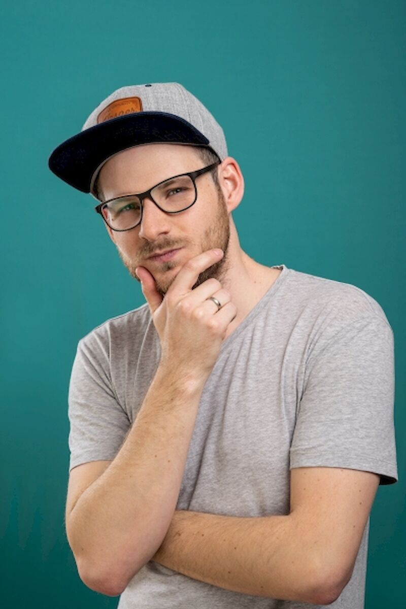 Ein Mann in grauen Klamotten schaut überlegend in die Kamera.