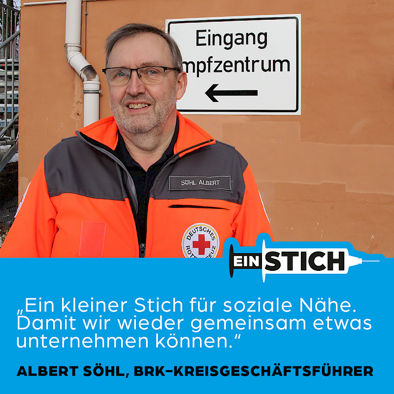 Mann in roter Jacke des Roten Kreuzes vor einem Impfzentrum.