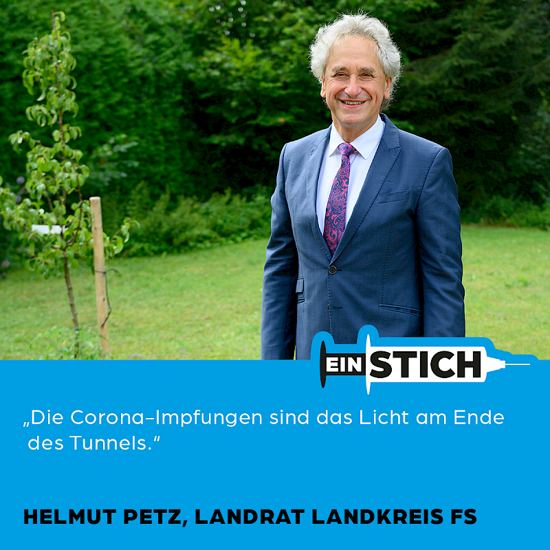 Mann im Anzug und Krawatte steht draußen vor einer grünen Landschaft.