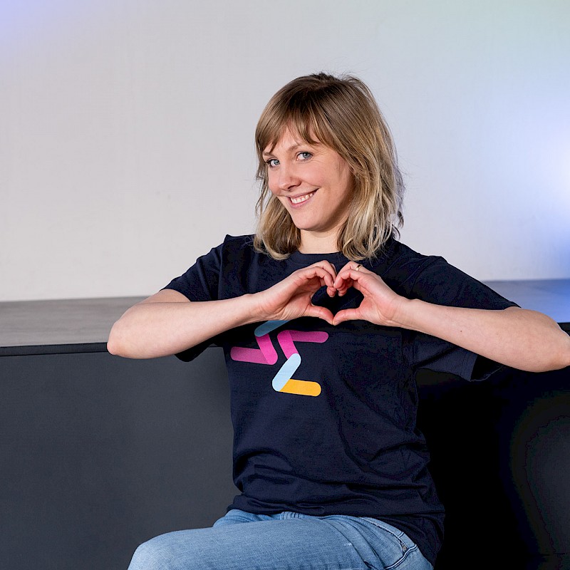 Frau im Motion Makers T-Shirt formt ein Herz mit ihren Händen und lächelt