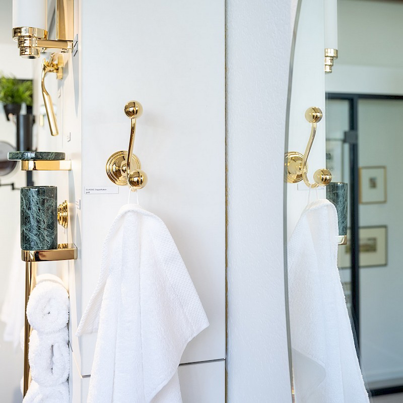 Detailaufnahme eines modernen Badezimmers mit goldenen Handtuchhaltern und Accessoires