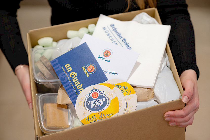 Eine Person hält einen Karton mit Produkten und Werbematerial von Schneider Weisse.