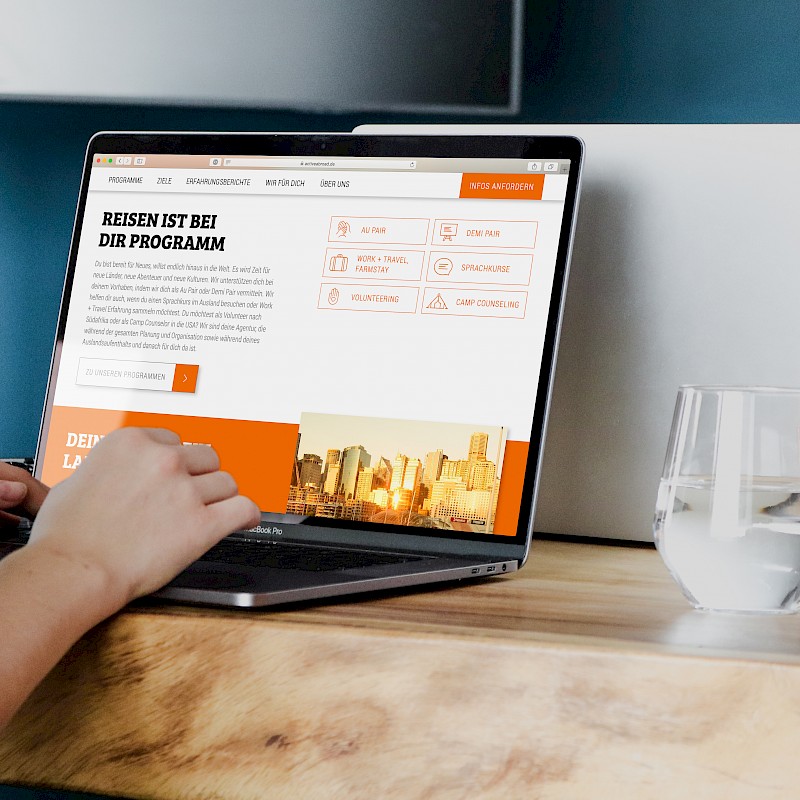 Person arbeitet an einem Laptop mit der 'active abroad'-Webseite, daneben ein Glas Wasser