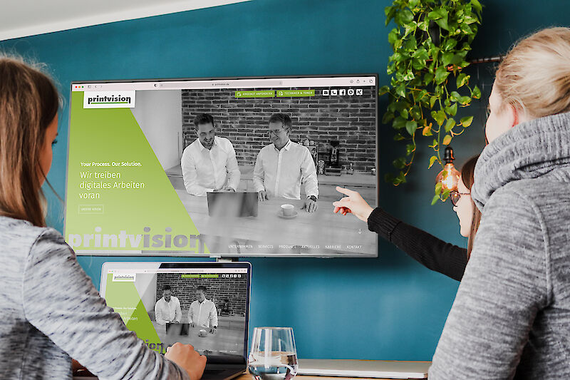 Personen zeigen auf einen Bildschirm mit der Webseite von Printvision