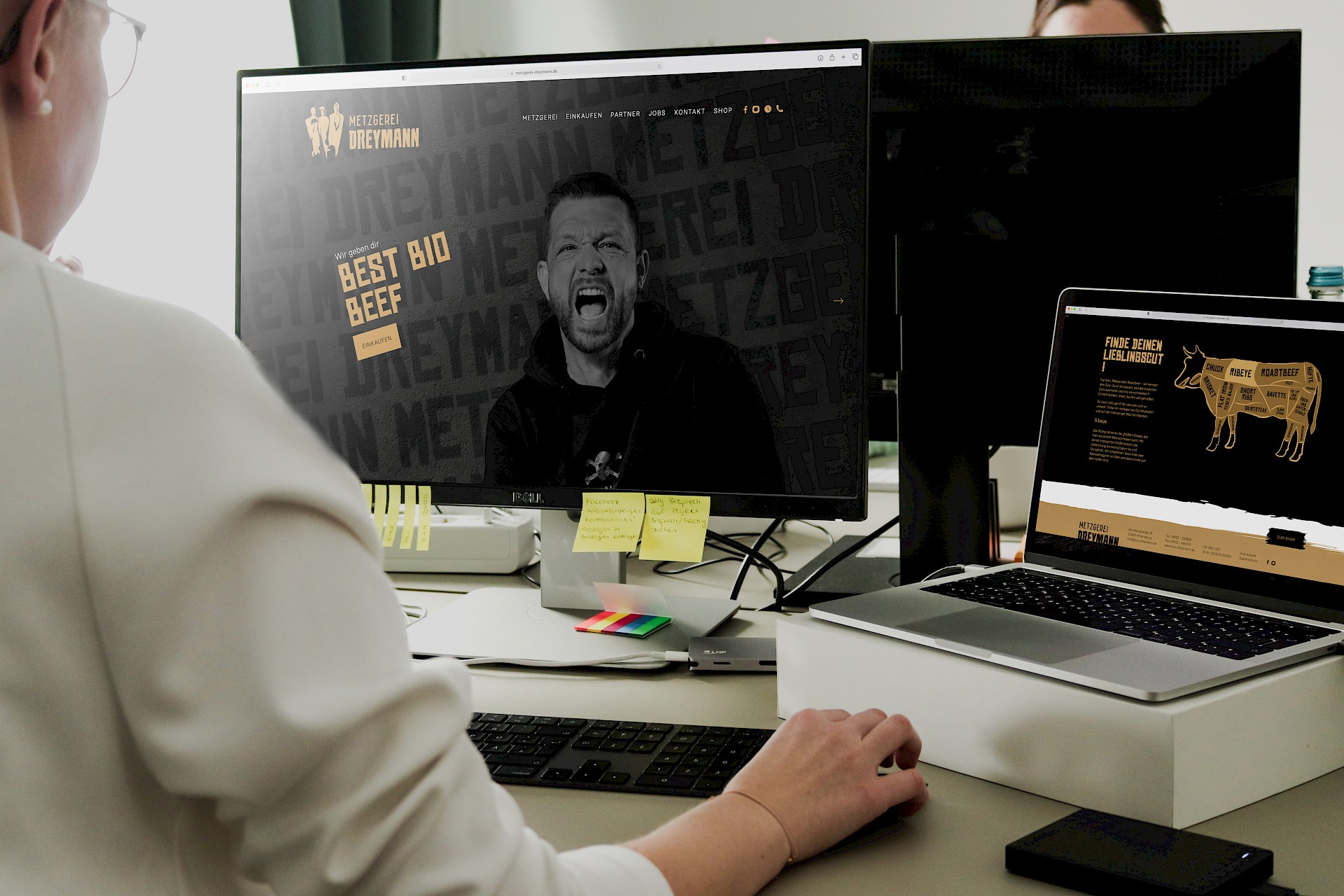 erson arbeitet am Computer, auf dem Bildschirm ist die Website der Metzgerei Dreymann mit dem Slogan 'Best Bio Beef' zu sehen."