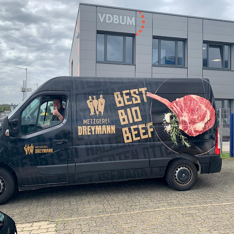 Schwarzer Van mit der Beschriftung "Best Bio Beef" steht vor einem Gebäude.