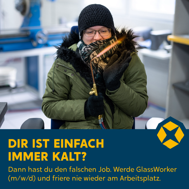 Eine frierende Frau ist eingewickelt in grüner Jacke und Schal, auf ihrem Kopf ist eine schwarze Mütze.