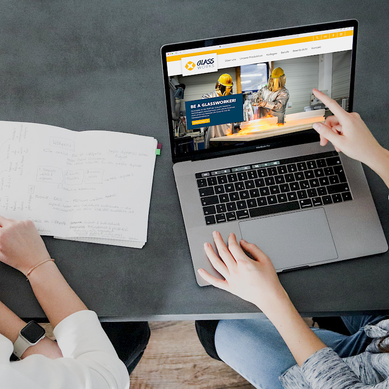 Zwei Personen besprechen sich und deuten auf ihren Laptop.