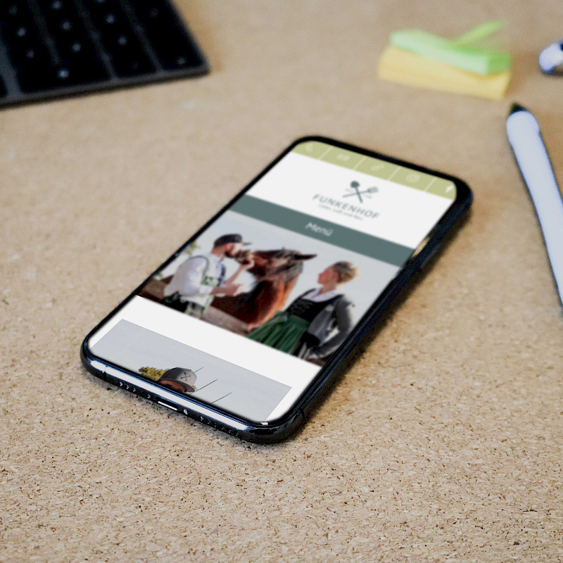 Auf einem Tisch liegt eine Handy, auf dem die Website "Funkenhof" zu sehen ist.