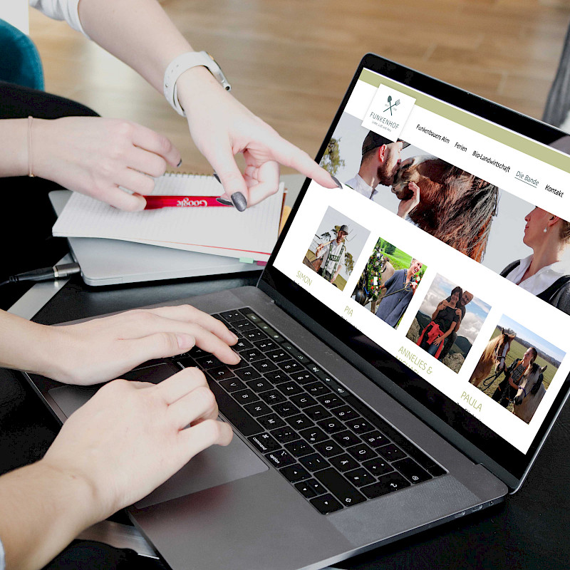 Zwei Personen deuten auf einen geöffneten Laptop.