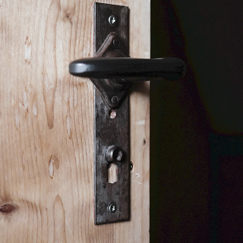 Eine offene Holztür mit schwarzem Türgriff.