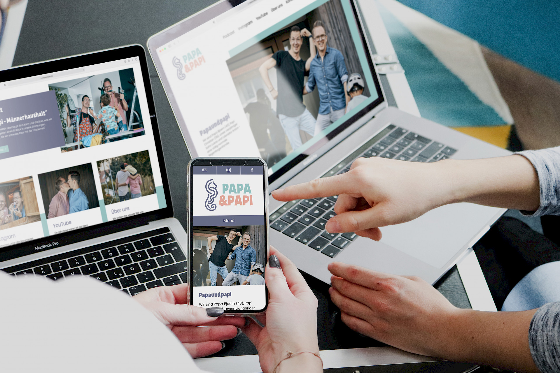 Zwei Personen bedienen zwei Laptops und ein Handy, auf welchen die Website von Papi & Papi geöffnet ist.