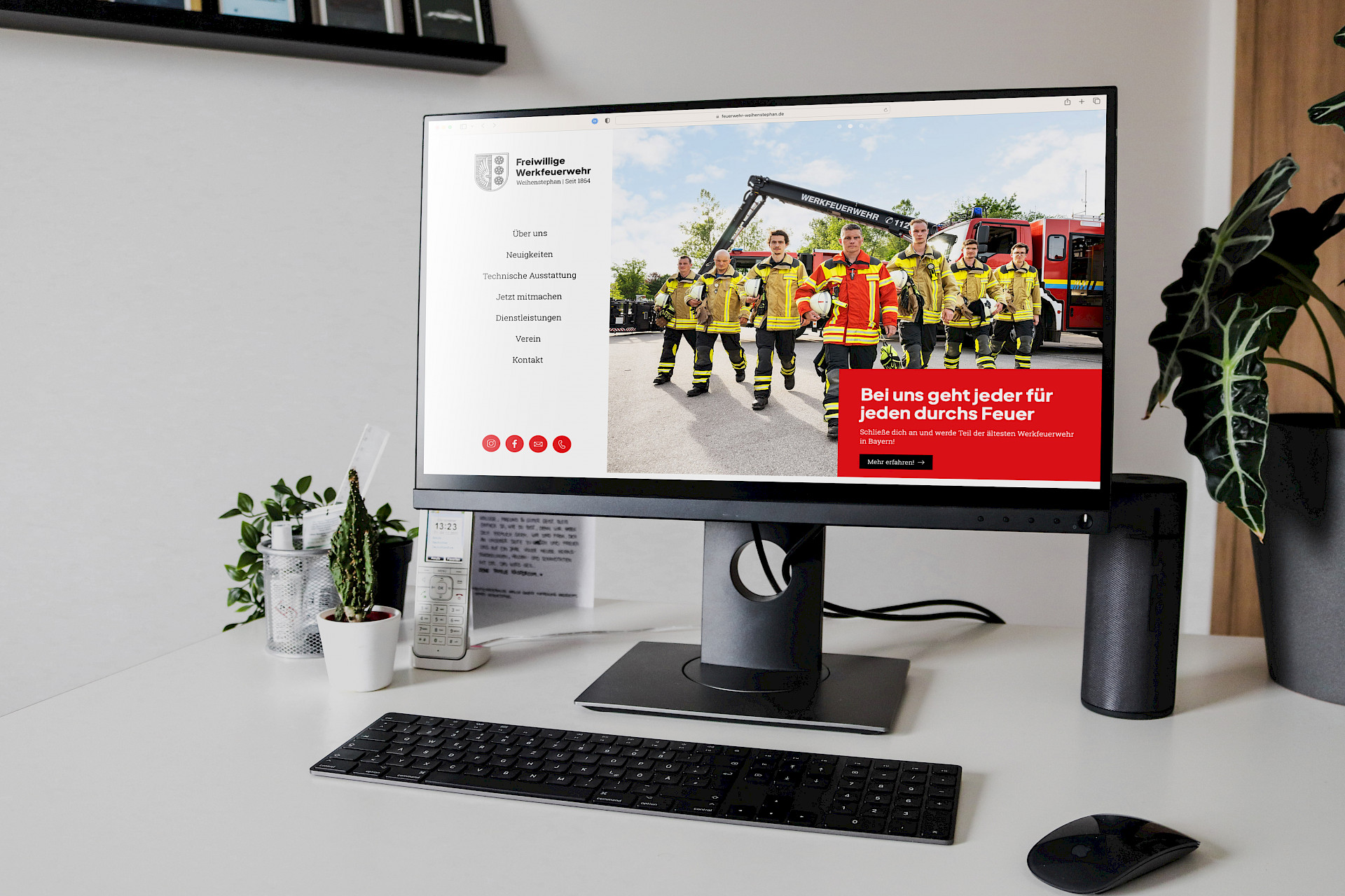 Website der Freiwilligen Feuerwehr auf einem Bildschirm, mit Feuerwehrleuten in voller Ausrüstung vor einem Feuerwehrauto