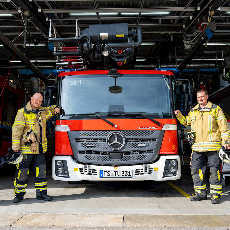 Zwei Feuerwehrmänner stehen neben ihrem Feuerwehrfahrzeug.