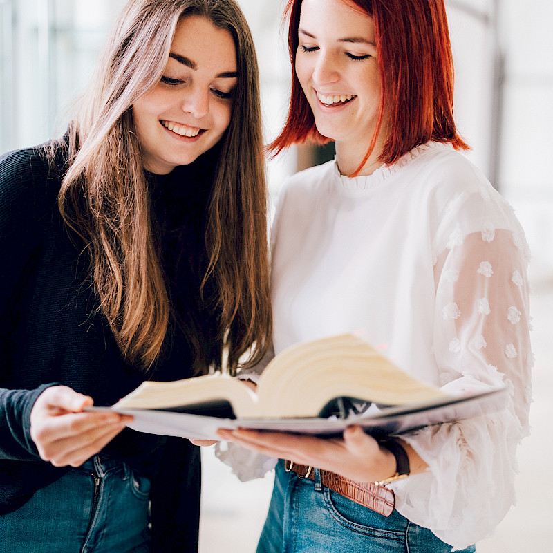 Zwei Frauen blättern gemeinsam durch ein Buch.