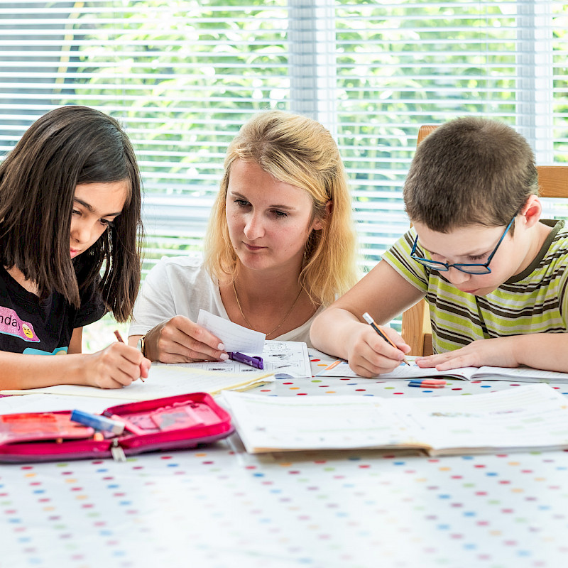 Zwei Junge Kinder die für die Schule lernen, während die Mutter daneben sitzt und Karteikarten abfragt