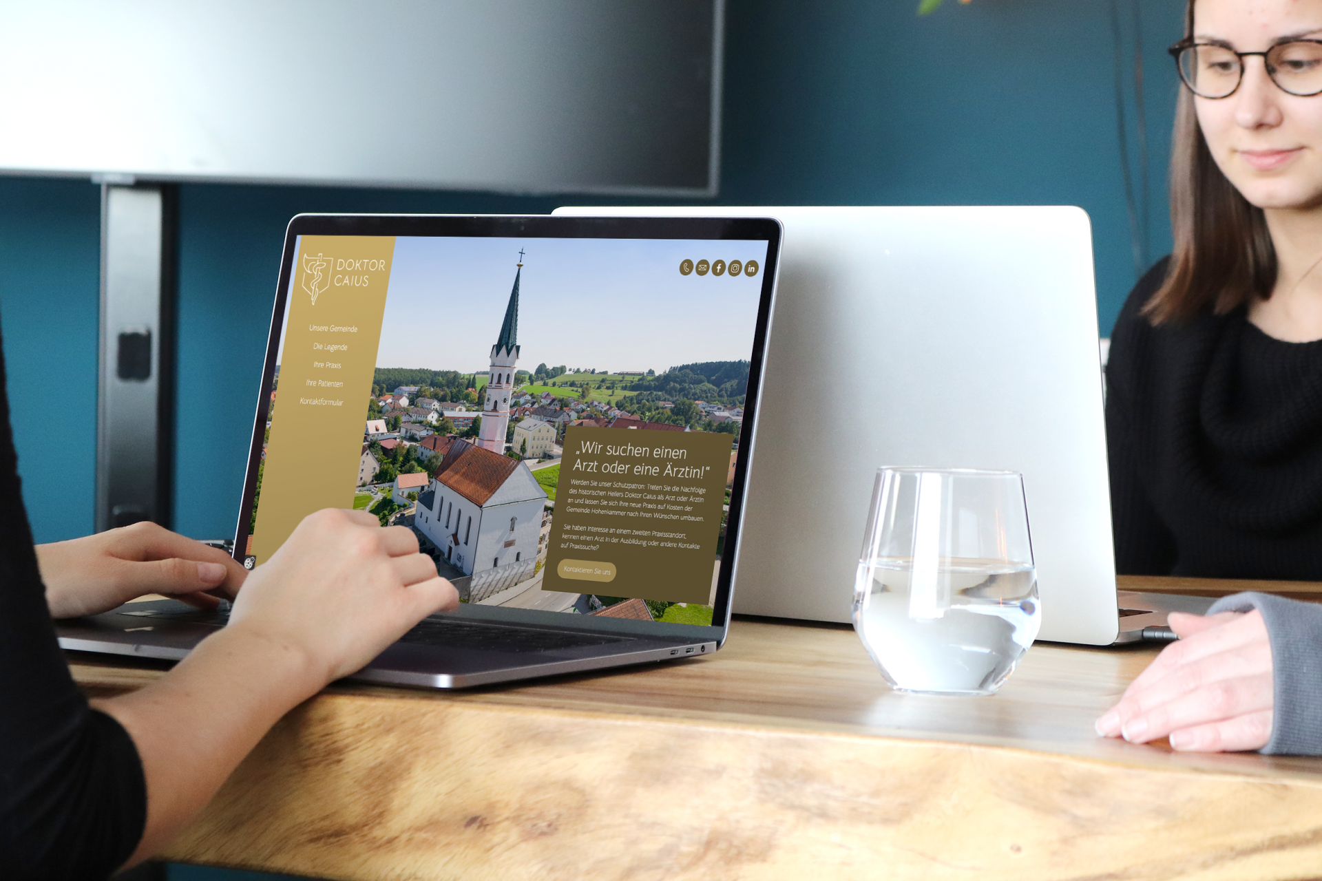 Zwei Personen arbeiten an Laptops, einer zeigt eine Webseite mit einer Arztsuche