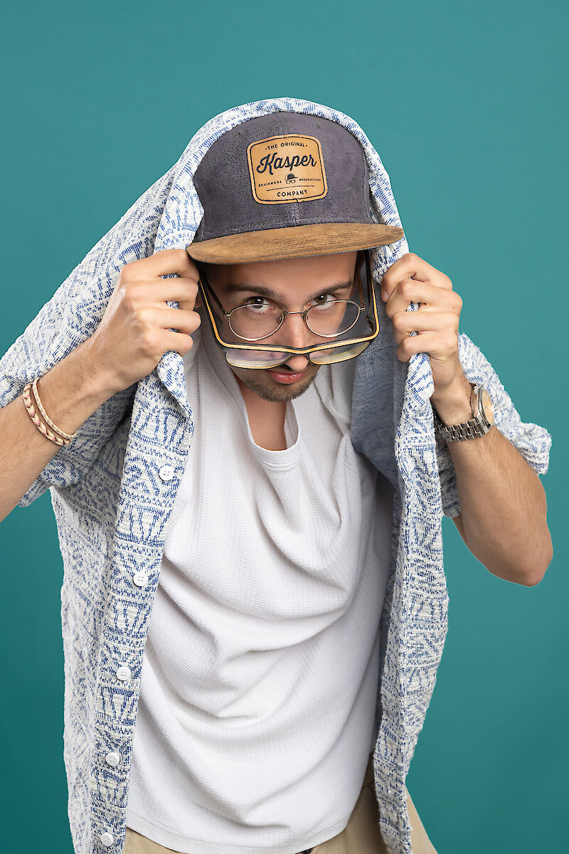 Mann mit Brille und Cap versucht sich unter seinem Hemd zu verstecken